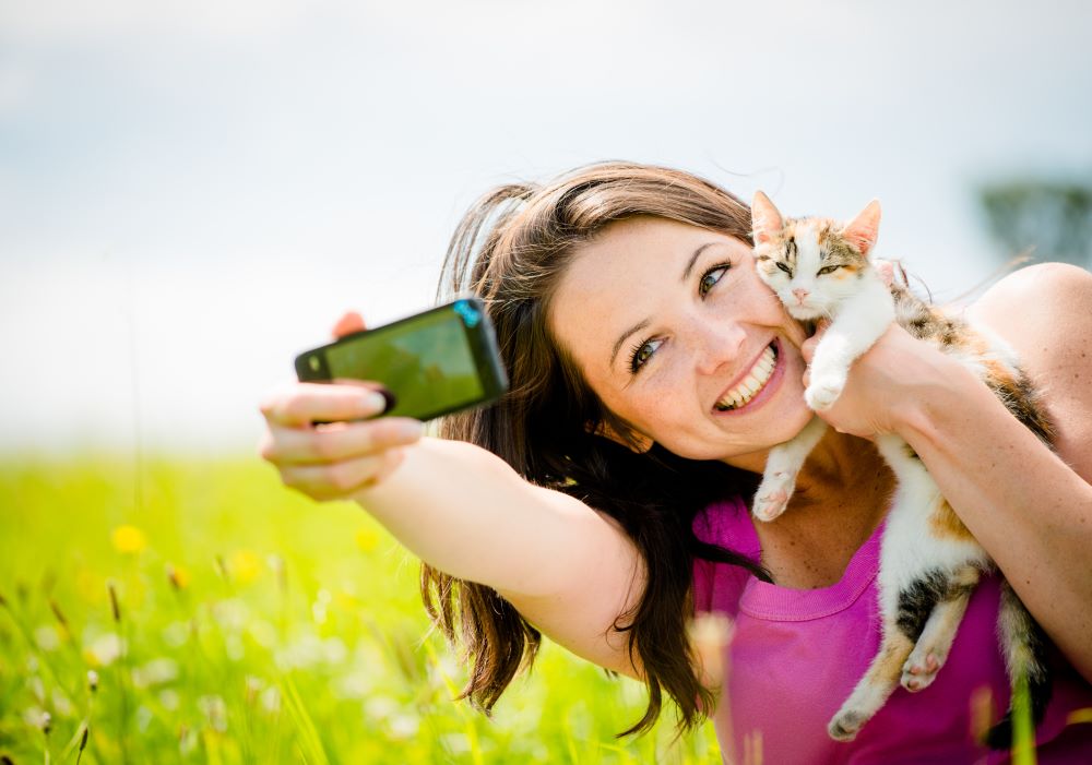 Woman taking photo with mobile phone camera of herself and her cat - outdoor in nature